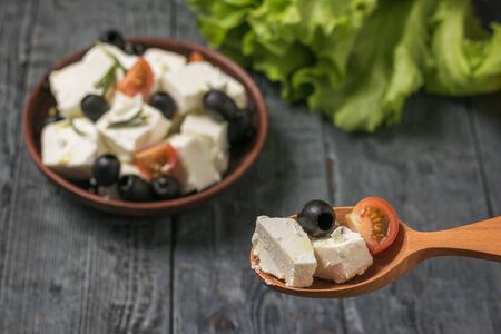 Wooden spoon with slices of cheese and tomatoes on the background of a plate with salad. Salad with cheese and vegetables.の写真素材