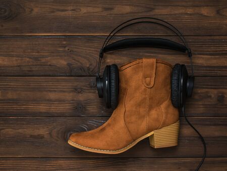 Suede boot with earbuds on a wooden background. Concept of folk music.