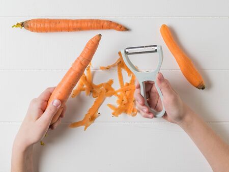 The child is engaged in cleaning carrots with a vegetable peeler. Cleaning carrots with a special...