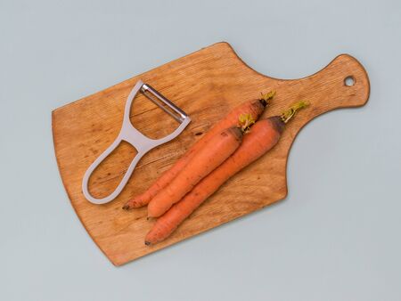 Three carrots and a peeler on a cutting Board on a blue background. Speciale quipment f or c leaning vegetables .の写真素材