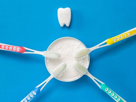 Tooth powder, four silicone toothbrushes, and a tooth figurine on a blue background. Means to care for the oral cavity.の写真素材
