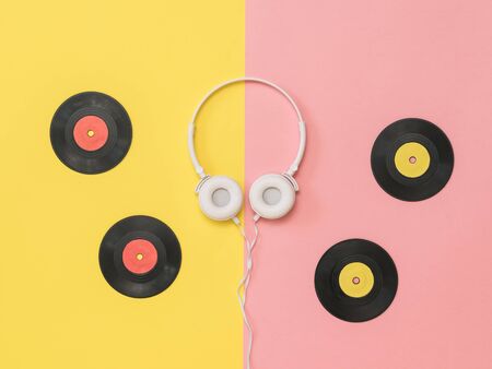 Four vinyl discs and white headphones on a pink and yellow background. Retro technique for playing music.の写真素材