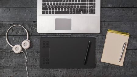 Laptop, graphic tablet, headphones and notebook on a wooden background. A device for working in...