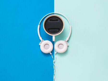 A Cup of coffee and white headphones on a two-tone background. Minimalism.