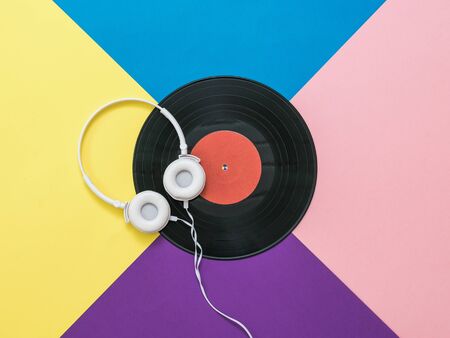 White headphones with a wire and a vinyl disc on a multicolored background. Retro technique for playing music.の写真素材