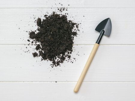 A shovel with a wooden handle and some fertile soil on a wooden background. Gardening.