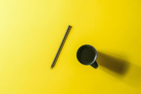 Black coffee Cup and black pencil on a yellow background. Minimalism.の写真素材