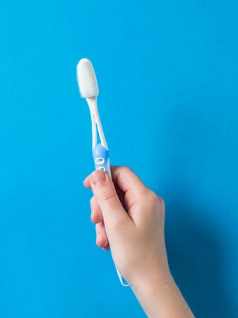 A child's hand with a blue toothbrush on a blue background. Means to care for the oral cavity.の写真素材
