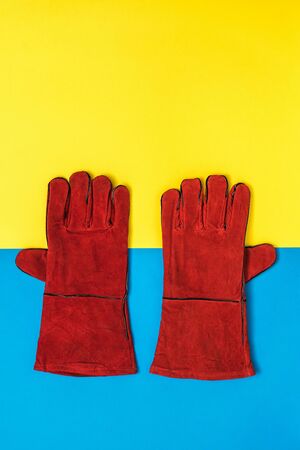 A pair of red welder's gloves on a yellow and blue background. Protective accessory for welding...