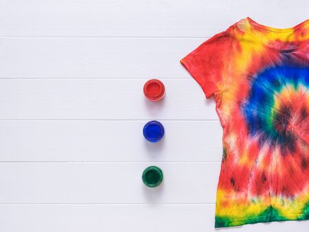 Three cans of paint and a tie dye t-shirt on a white wooden background. White clothes painted by hand. Flat lay. Place for text.の写真素材