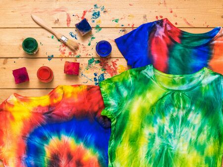 Three tie dye t-shirts on a wooden background with paint. White clothes painted by hand. Flat lay. Place for text.の写真素材