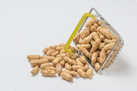 Peanuts fall out of a grocery basket on a white wooden table. Fresh crop of peanuts.の写真素材