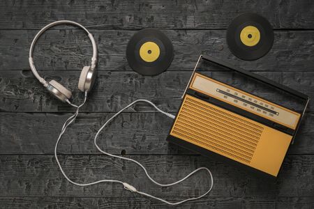 Retro radio with headphones and yellow vinyl discs on a wooden background. Radio engineering of the past time. The view from the top.の写真素材