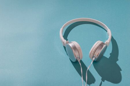 Headphones with a wire in hard light on a blue background. Mobile audio playback equipment.