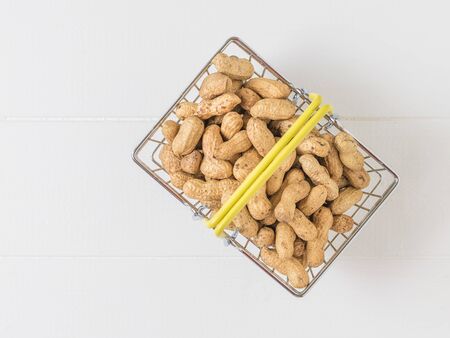Top view of a basket of peanuts on a white wooden table. Fresh crop of peanuts.