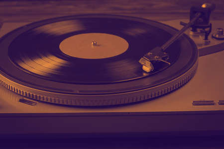 Tinted image of a vinyl record player on a wooden background. Music on vinyl discs.