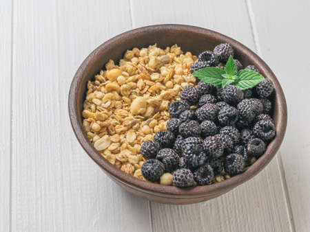 Granola and black raspberries in a clay bowl on a white table. The dish is rich in fiber.