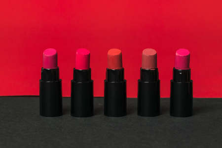 Five bottles of lipstick on a red and black background. Cosmetics for lips.