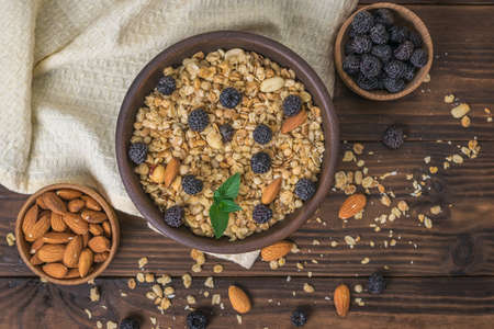 Granola with black raspberries and almonds on a cloth on a wooden table. The dish is rich in fiber.
