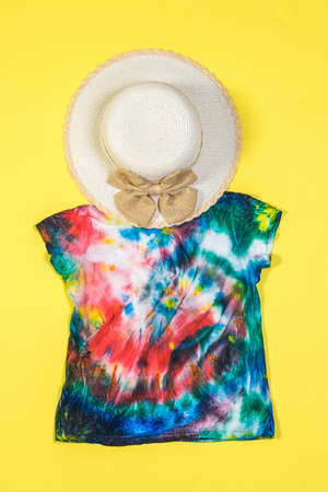 A large hat and tie dye t-shirt on a yellow background. White clothes painted by hand. Flat lay.の写真素材