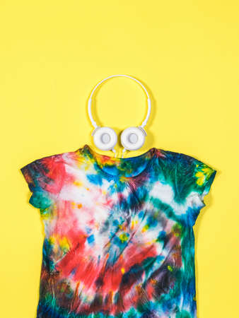 White headphones and a tie dye t-shirt on a yellow background. White clothes painted by hand. Flat lay.の写真素材