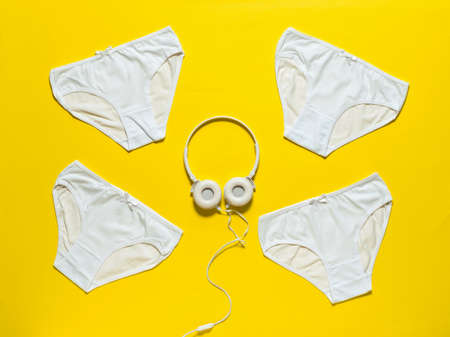 Set of four white panties and white headphones on a yellow background. Underwear. The view from the top. Beautiful lingerie. Flat lay.の写真素材