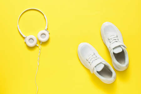 Headphones and sneakers are white on a bright yellow background. The concept of a healthy lifestyle and music.の写真素材