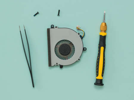 A screwdriver, tweezers, and a dismantled laptop cooling fan. Repair and restore laptop performance.
