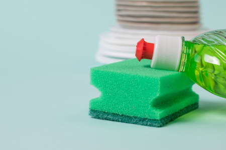 Dish washing gel and foam sponge on the background of plates. The concept of cleaning and...