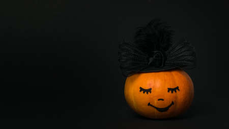 Pumpkin in a black hat with a woman's face on a black background. Halloween party.の写真素材