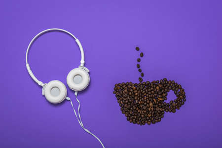 A Cup of coffee made from coffee beans and white headphones on a lilac background. The concept of coffee and music.の写真素材