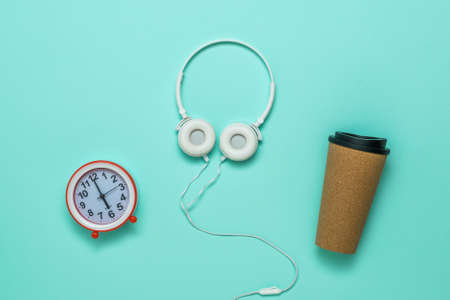 Headphones, a paper coffee Cup and an alarm clock on a blue background. Accessories to start the day.の写真素材