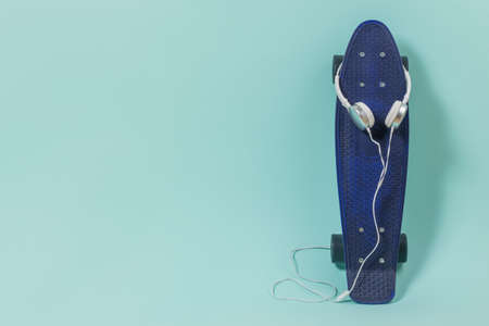Blue skateboard and white headphones on a blue background. Sports style. Place for text.の写真素材