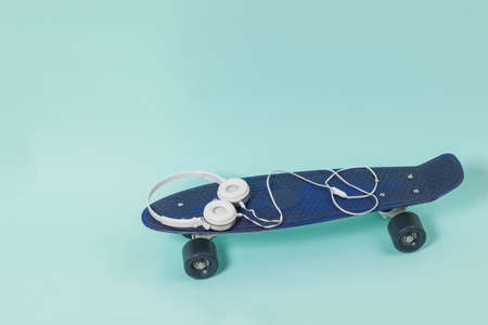 White headphones lying on a blue skateboard on a light background. Sports style. Place for text.