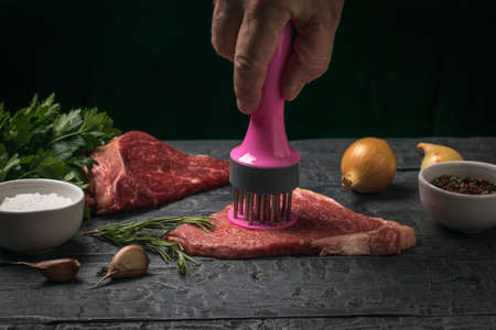 A man prepares a beef steak using a special device. Cooking meat dishes.