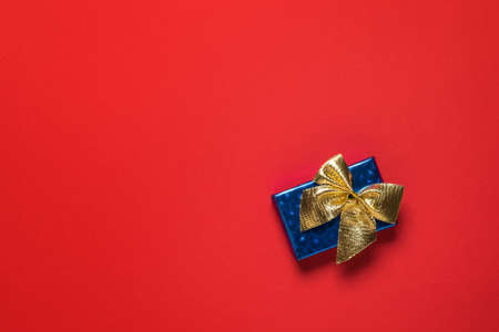 Blue gift box with a gold bow on a red background. A surprise gift.の写真素材