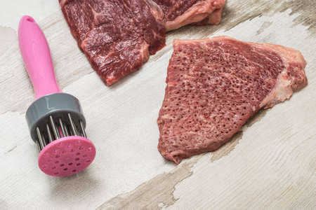 The process of cooking beef chops and a special device on a wooden background. Meat dish.