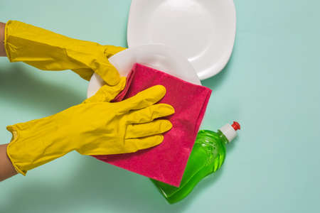 Hands in rubber gloves wipe clean dishes with a red cloth. Homework. Washing dishes by hand.の写真素材