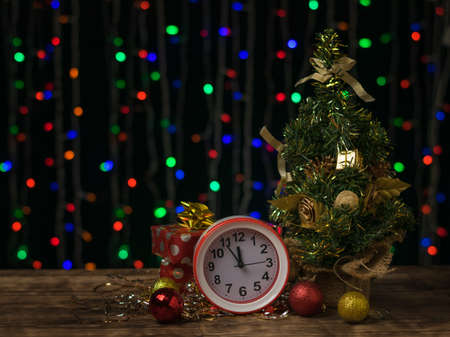 Alarm clock near a small Christmas tree with gifts. Meeting of Christmas and new year.