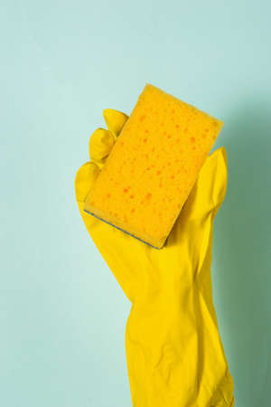 A hand in a rubber glove holds a foam sponge on a blue background. Homework. Washing dishes by hand.の写真素材