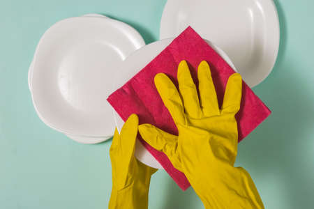Hand in rubber gloves wiping with a clean, white dishes. Homework. Washing dishes by hand.