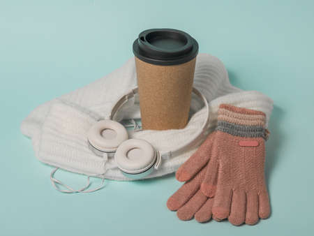 Coffee Cup, gloves, scarf and headphones on a blue background. Winter mood.
