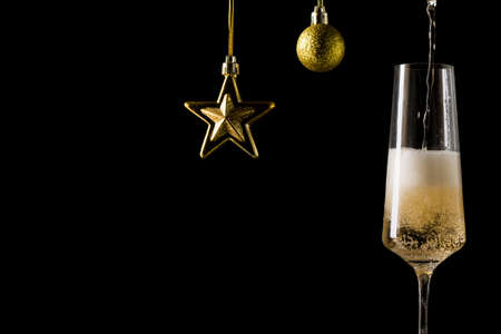 Filling a glass of champagne and decorations in the form of a star and a ball on blackの写真素材
