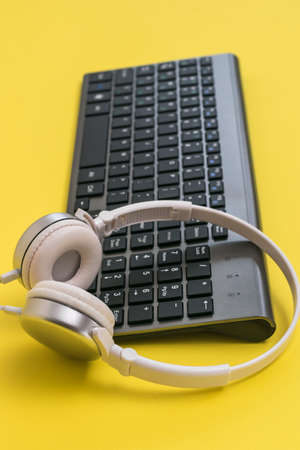 Classic wireless keyboard and white headphones on a yellow background. Peripheral devices for the computer.の写真素材
