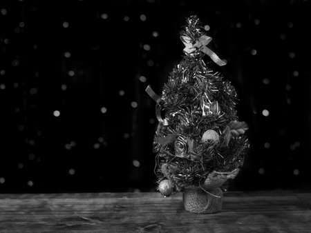 Black and white image of a Christmas tree on a wooden table on a black background. Christmas and New year celebrations. Space for text.の写真素材