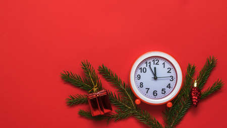 Green spruce branches and a red alarm clock on a red background. Meeting of Christmas and new year.