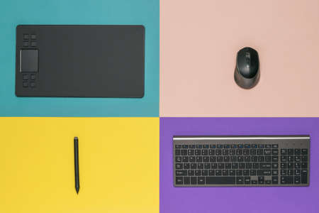 Graphic tablet, wireless keyboard and mouse on a four-color background. The tools of a designer.