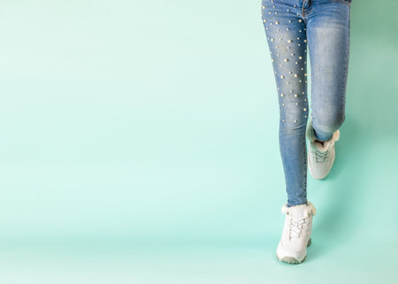 Legs in tight jeans and white winter sneakers against the blue wall.の写真素材
