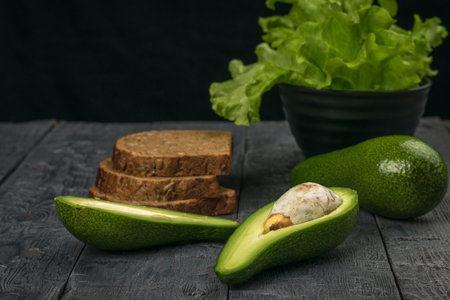 Avocado fruit and bread made from coarse flour on a black wooden table. Vegetarian food.の写真素材