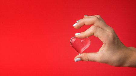 The girl's hand gently holds a glass heart on a red background. A symbol of love and life.の写真素材
